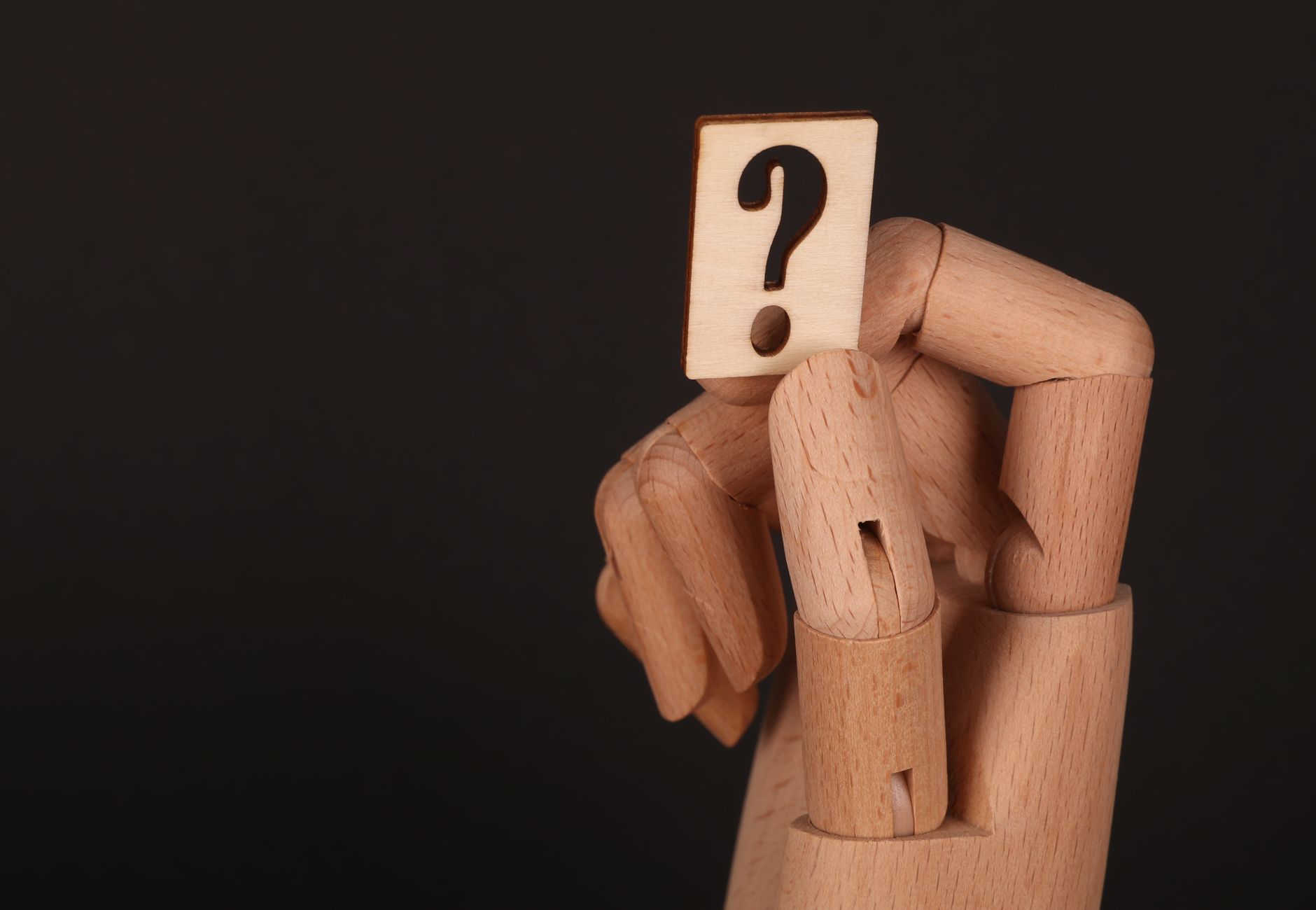 Close-up of a wooden mannequin hand holding a block with a question mark, emphasizing curiosity.